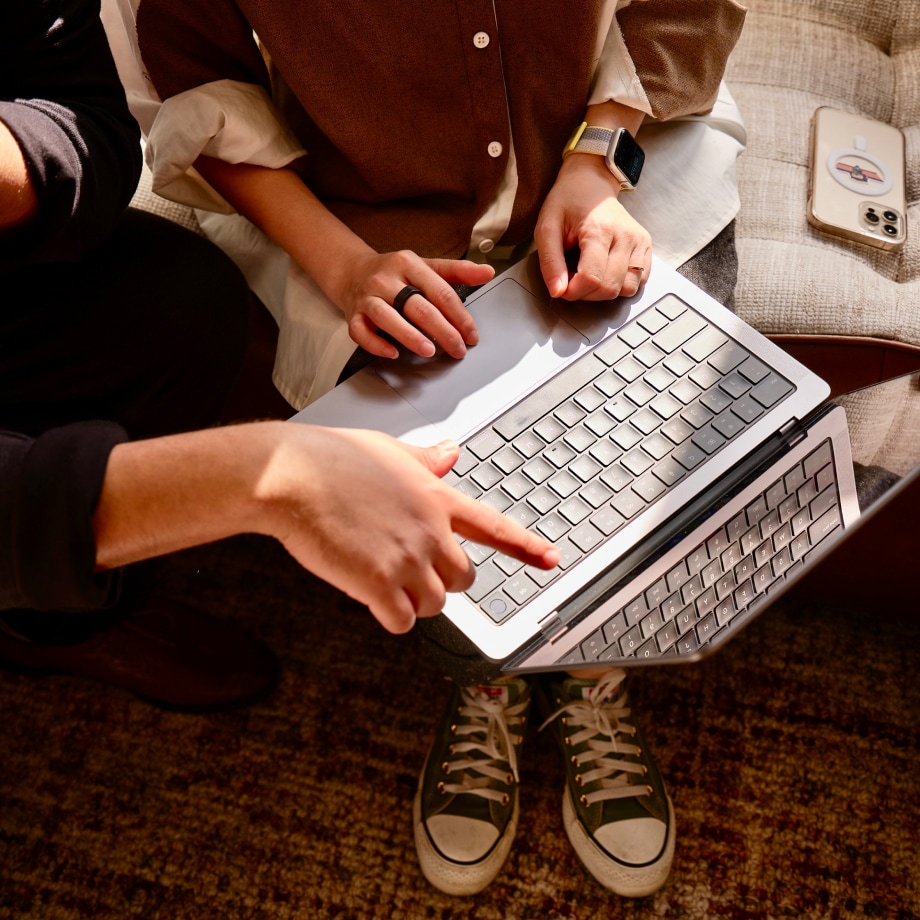 Two people huddled around a laptop engaging in a discussion, while one person points at screen