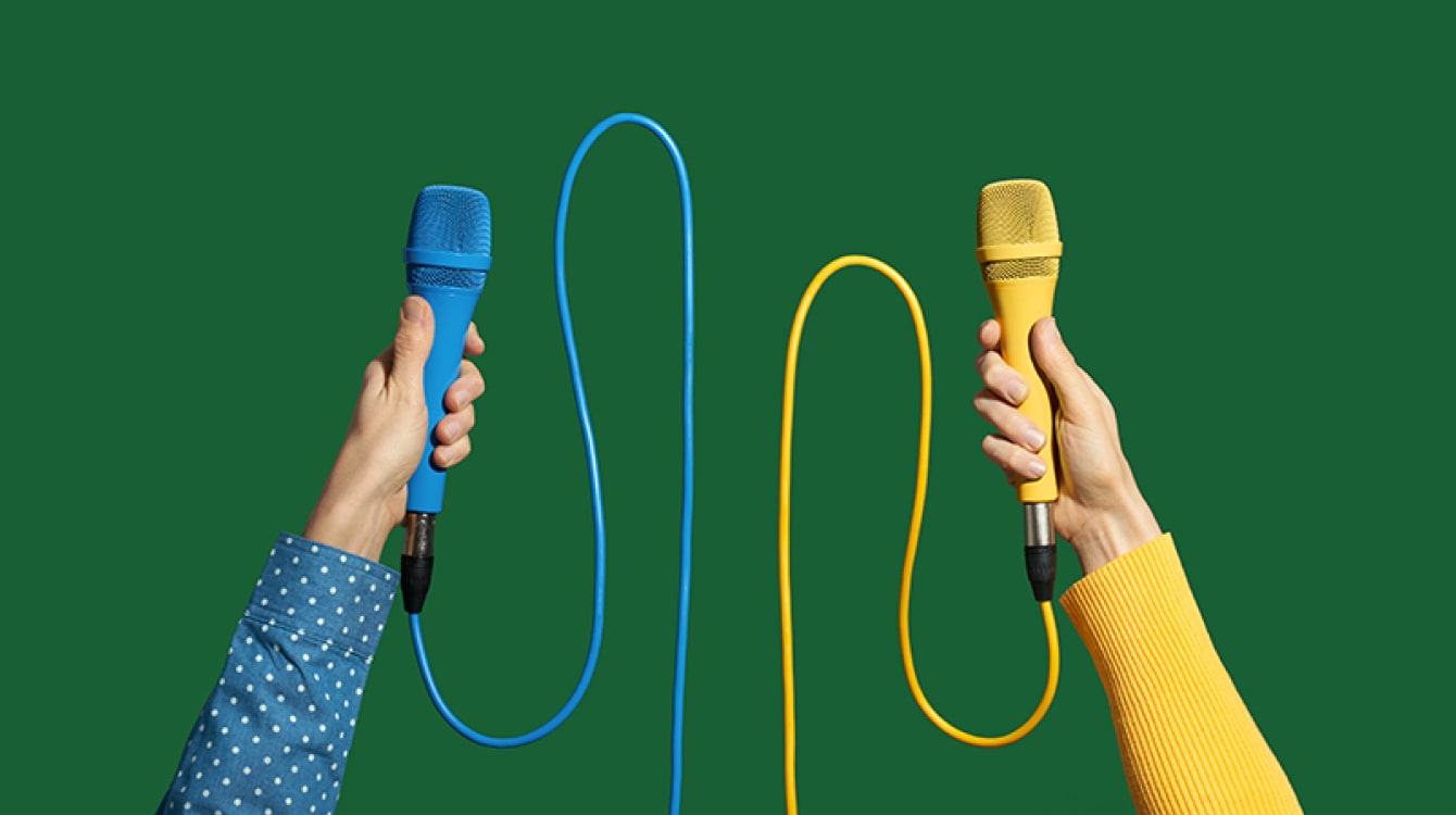 Two hands holding different colored microphones representing leaders discussing the new way of work