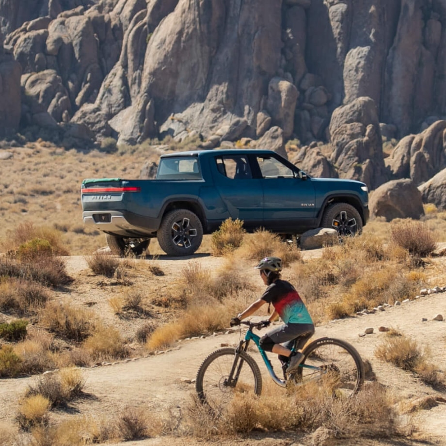 Vehículo Rivian en un paisaje frondoso con unos ciclistas andando al frente